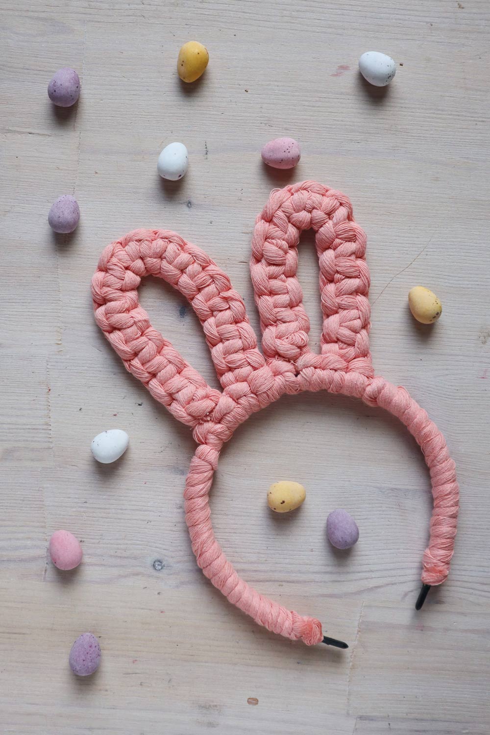 DIY macrame bunny  ears headband in pink, surrounded by pastel colour chocolate eggs
