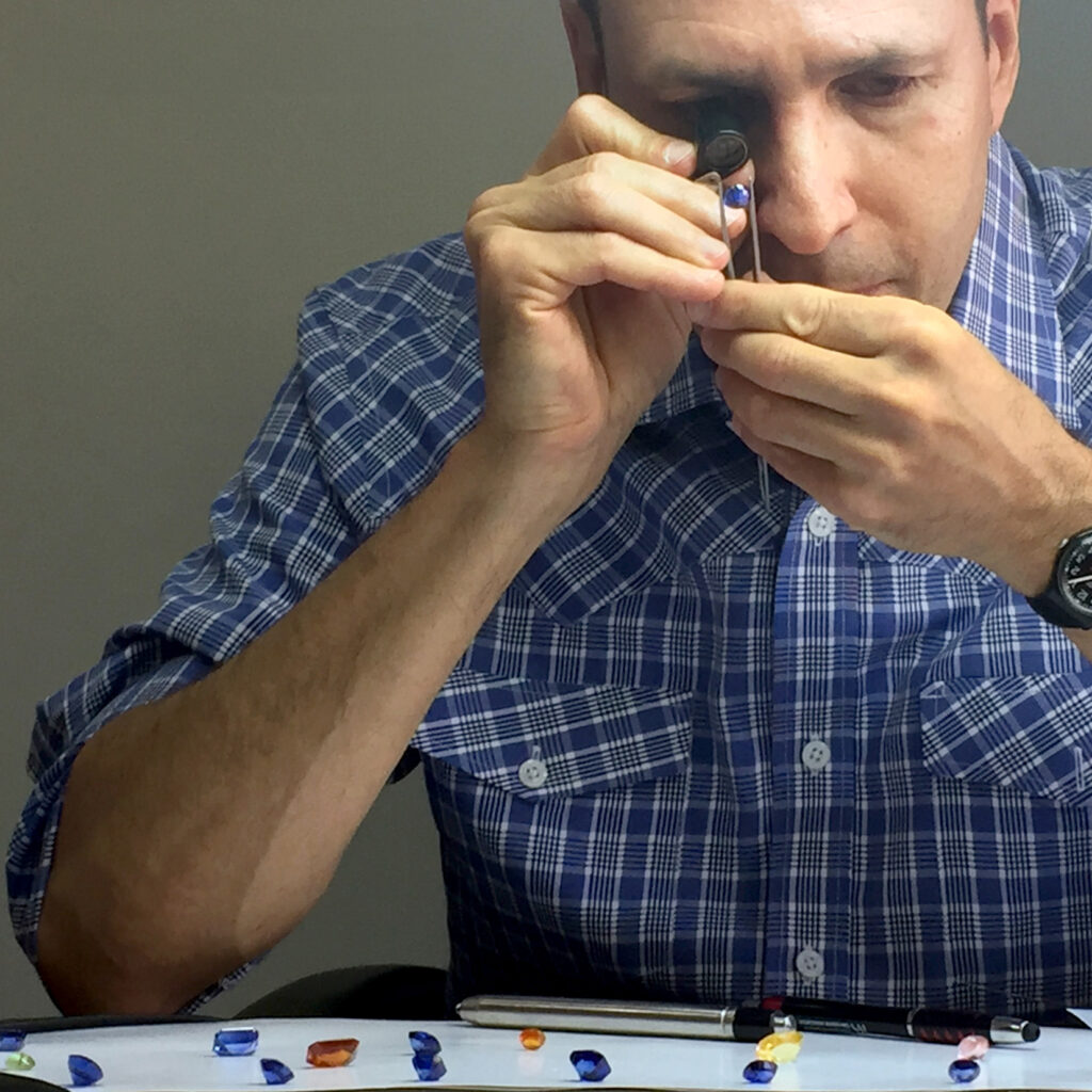 A white male in a blue golf shirt analyses coloured gemstones.
